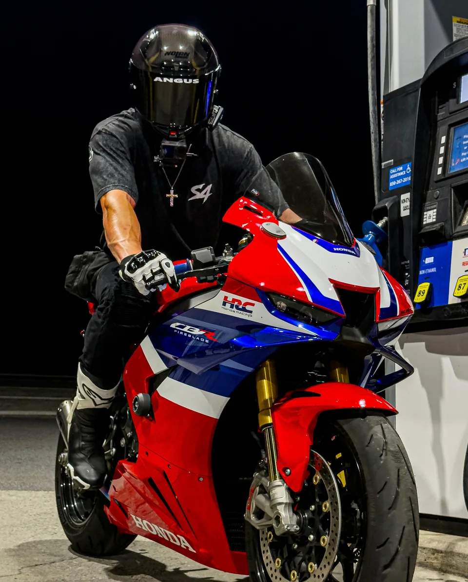 Ricky in a black helmet on his red, white, and blue Honda Fireblade at a gas station at night